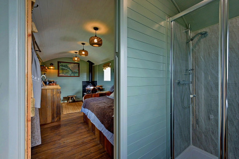 Interieur van de mobiele woning 'Joan' Shepherds Hut in het VK met douchecabine, bed en houten vloer.
