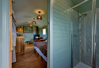 Interieur van de mobiele woning 'Joan' Shepherds Hut in het VK met douchecabine, bed en houten vloer.