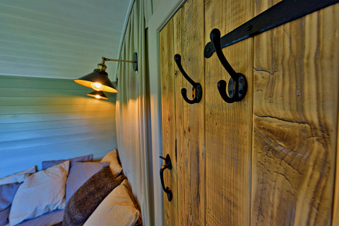 Interieurbeeld van Joan Shepherds Hut met houten panelen, haken en een knus bed in het tiny house.