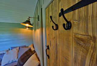 Interieurbeeld van Joan Shepherds Hut met houten panelen, haken en een knus bed in het tiny house.