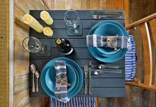 Tavola apparecchiata per due con piatti blu, tovaglioli a righe e candele al mobil home 'Susanna' Poachers Hut UK.