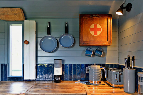 Accogliente cucina in casa mobile con piano in legno, pentole blu e armadietto con croce rossa.