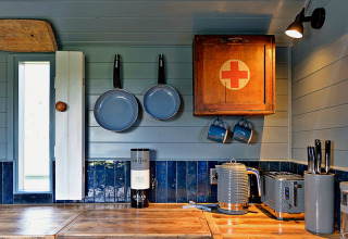 Accogliente cucina in casa mobile con piano in legno, pentole blu e armadietto con croce rossa.