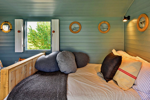Accogliente zona notte nella 'Susanna' Poachers Hut con cuscini e pareti in legno, Regno Unito.