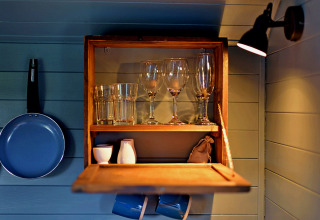 Interno di casa mobile con mensola in legno, bicchieri, tazze e padella blu appesa alla parete.