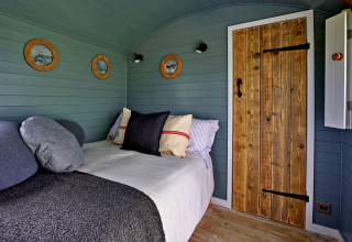 Interno di una roulotte accogliente con porta di legno, pareti verdi, oblò rotondi e letto con cuscini.