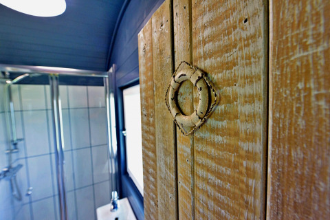 Primo piano di una porta rustica in legno con anello metallico, doccia sullo sfondo, casa mobile.