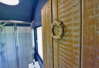 Primo piano di una porta rustica in legno con anello metallico, doccia sullo sfondo, casa mobile.