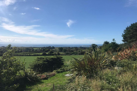 Vista da un alloggio glamping su campi verdi, alberi e il mare in lontananza sotto un cielo sereno.