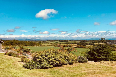 Beautiful view of rolling green countryside from a glamping accommodation under a bright blue sky.
