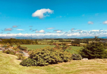 Wunderschöner Blick auf grüne Felder und Hügel von einer Glamping-Unterkunft unter blauem Himmel.
