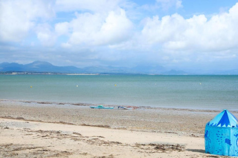 Scena di spiaggia in un campeggio glamping con tenda blu in primo piano e mare con montagne sullo sfondo.