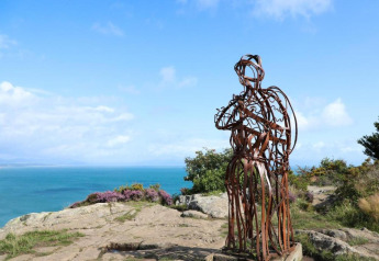 Metallskulptur auf Felsen mit Meerblick unter blauem Himmel, aufgenommen bei einer Glamping-Unterkunft.