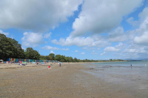 Spiaggia con cabine colorate, persone che passeggiano e si rilassano sotto un cielo azzurro nel Regno Unito.