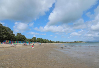 Spiaggia con cabine colorate, persone che passeggiano e si rilassano sotto un cielo azzurro nel Regno Unito.