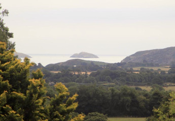 View from a glamping site overlooking green fields, hills, and distant islands on a cloudy day.