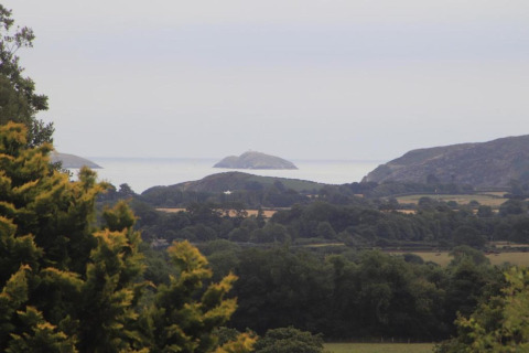 View from a glamping site overlooking green fields, hills, and distant islands on a cloudy day.