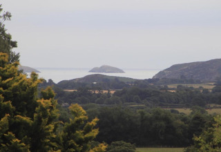 Vista da una sistemazione glamping su campi verdi, colline e isole distanti in una giornata nuvolosa.
