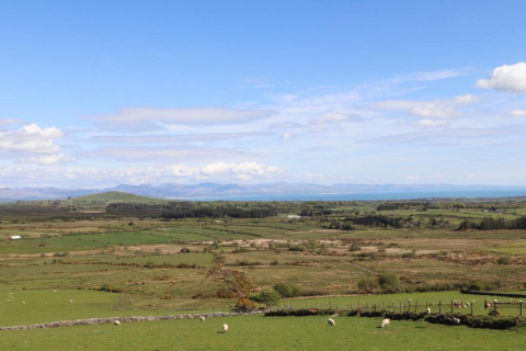Vista da un alloggio glamping su campi verdi, colline lontane e un cielo azzurro con alcune nuvole.
