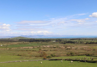View from a glamping accommodation overlooking open green fields, distant hills and a bright blue sky.