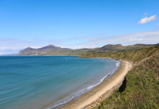 Vista da un glamping su una baia tranquilla, spiaggia sabbiosa e colline verdi sotto un cielo azzurro limpido.