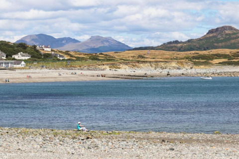 Alloggio glamping sul mare con montagne sullo sfondo e ospiti che si rilassano sulla spiaggia.