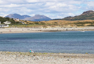 Alloggio glamping sul mare con montagne sullo sfondo e ospiti che si rilassano sulla spiaggia.