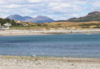 Blick auf eine Glamping-Unterkunft am Meer mit Bergen im Hintergrund und Menschen am Strand.