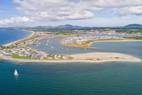 Vue d'un parc de mobil-homes en bord de mer, marina avec voiliers et montagnes en arrière-plan.