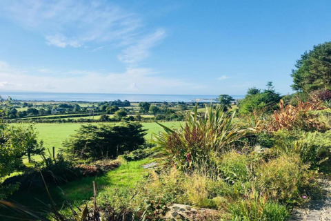 Belle vue depuis un hébergement glamping sur des champs verdoyants, des arbres et la mer sous un ciel bleu.
