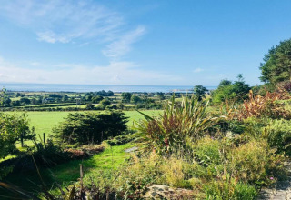 Splendida vista da un alloggio glamping con prati verdi, alberi e il mare sotto un cielo azzurro e limpido.