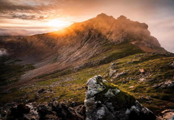 Prachtig berglandschap in avondlicht met zonnestralen over de ruige top en groene hellingen.