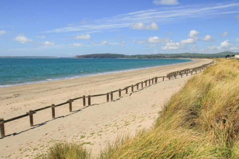 Photo of a sandy beach, blue sea, grassy dunes and sky, taken at a glamping accommodation.