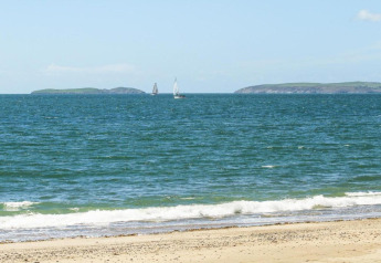 Zicht vanuit een mobiel huisje op een zandstrand, zeilboten, golven en eilanden aan de horizon.