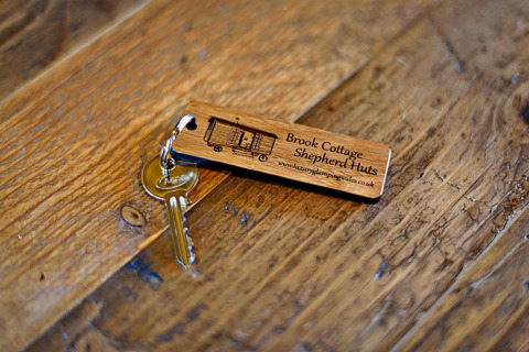 Una chiave con portachiavi in legno Brook Cottage Shepherd Huts su un tavolo rustico nel Regno Unito.