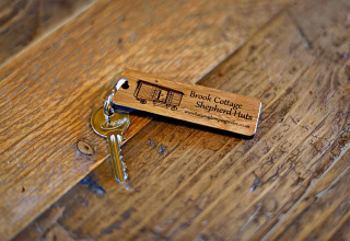 Una chiave con portachiavi in legno Brook Cottage Shepherd Huts su un tavolo rustico nel Regno Unito.