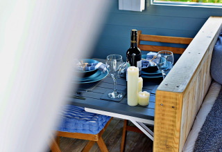 Tavola accogliente con vino, candele e piatti blu nel mobil home 'Susanna' Poachers Hut, Regno Unito.