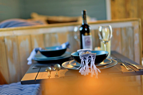 Tavola apparecchiata con piatti neri, bicchieri da vino e bottiglia nel mobil home 'Susanna' Poachers Hut, Regno Unito.
