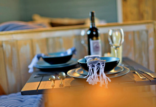 Tavola apparecchiata con piatti neri, bicchieri da vino e bottiglia nel mobil home 'Susanna' Poachers Hut, Regno Unito.