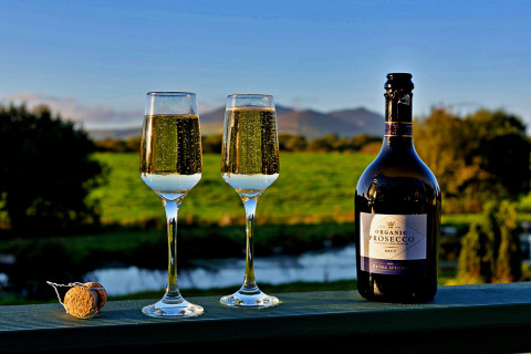 Due calici e una bottiglia di prosecco biologico su una ringhiera con vista verde a 'Susanna' Poachers Hut.