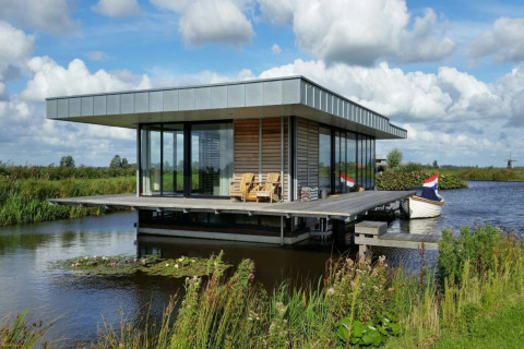 Moderne husbåd Watervilla de Blauwe Reiger ligger på vandet, omgivet af natur, med båd og udendørs siddeplads.
