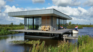 Moderna houseboat Watervilla de Blauwe Reiger sull’acqua, immersa nella natura, con pontile e seduta esterna.