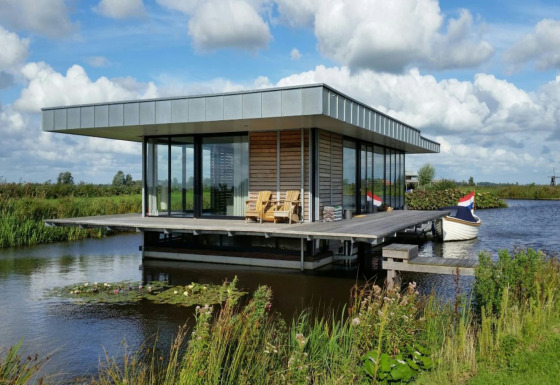 Moderne husbåd Watervilla de Blauwe Reiger ligger på vandet, omgivet af natur, med båd og udendørs siddeplads.