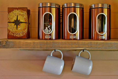 Shelf with three copper canisters and two hanging mugs in the cozy 'Marared' Gypsy Hut, United Kingdom.