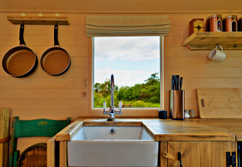 Küche in einem Tiny House mit Holztresen, Spüle, Fensterblick, Pfannen, Messerblock und Tasse.