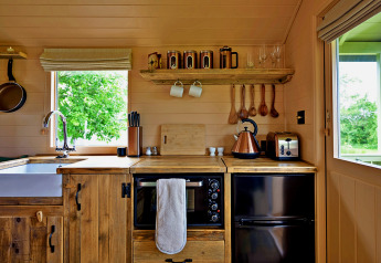 Gemütliche kleine Holzküche im 'Marared' Gypsy Hut, Großbritannien, mit ländlicher Einrichtung und Fensterblick.
