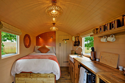 Gemütliches Tiny House 'Marared' Gypsy Hut im Vereinigten Königreich mit Bett, Holzdekor und Küche.