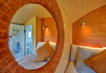 Cozy view of the bedroom in the 'Marared' Gypsy Hut, reflected in a round mirror, United Kingdom.