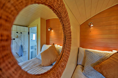 Cozy view of the bedroom in the 'Marared' Gypsy Hut, reflected in a round mirror, United Kingdom.