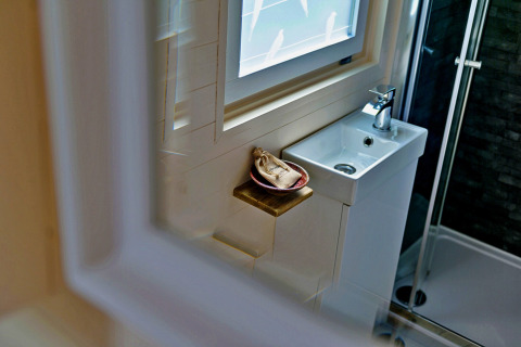 Compact bathroom in 'Marared' Gypsy Hut featuring a small sink, window, and shower in the United Kingdom.